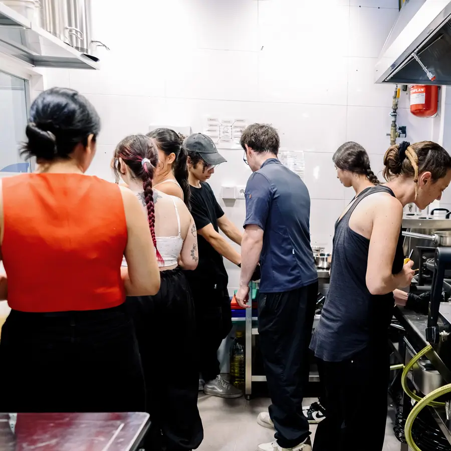 Parte del equipo trabaja de espaldas en la cocina del restaurante, entre fogones y campanas, durante un servicio.