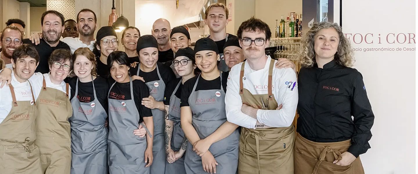 El equipo de Foc i Cor al completo, con delantales y gorros de cocina, delante del rótulo del restaurante.